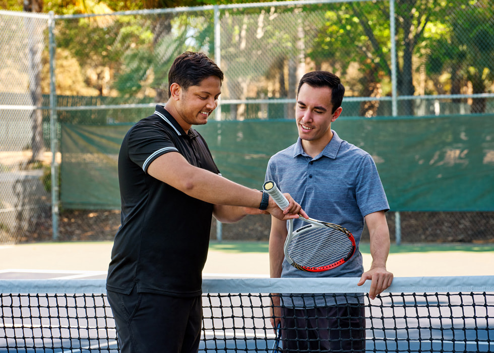 Sahai 在球场上向一位网球选手展示他的 Apple Watch。