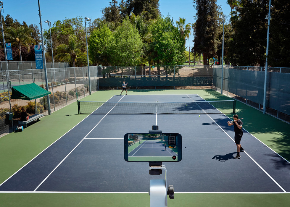 一台 iPhone 正在拍摄两名选手在球场上打网球。