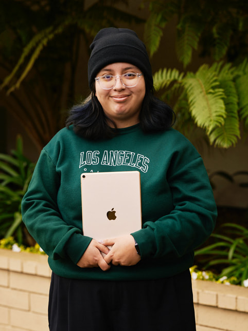 Exceptional Minds 学生 Angela Ibarra 的照片。Angela 身穿一件绿色运动衫，上面写着“加州洛杉矶”字样，戴着眼镜和黑色无檐帽。
