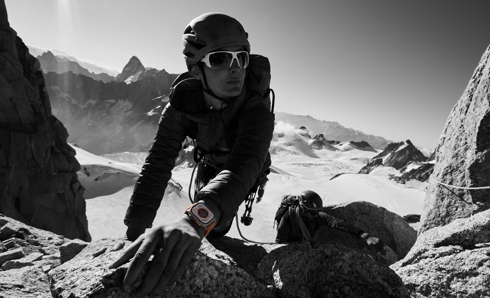 群山之中，一个人佩戴 Apple Watch Ultra 正在攀岩。