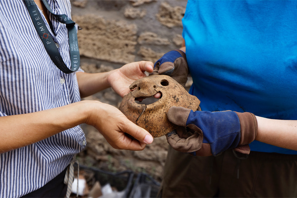 两位考古学者在发掘现场手持一副陶制面具。