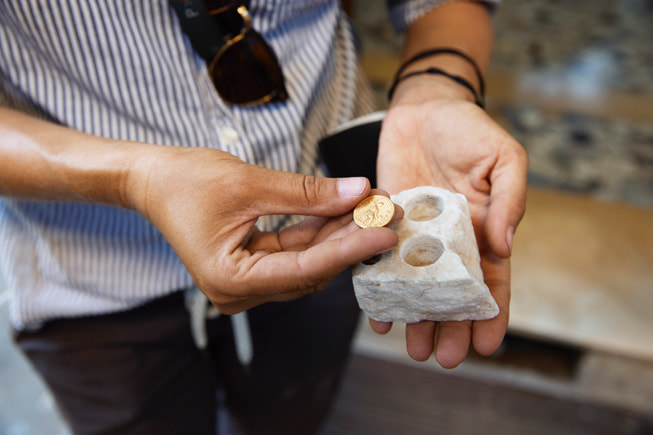 Emmerson 一手拿着金币，另一只手里举着一块石头，石头上有硬币形状的孔洞。