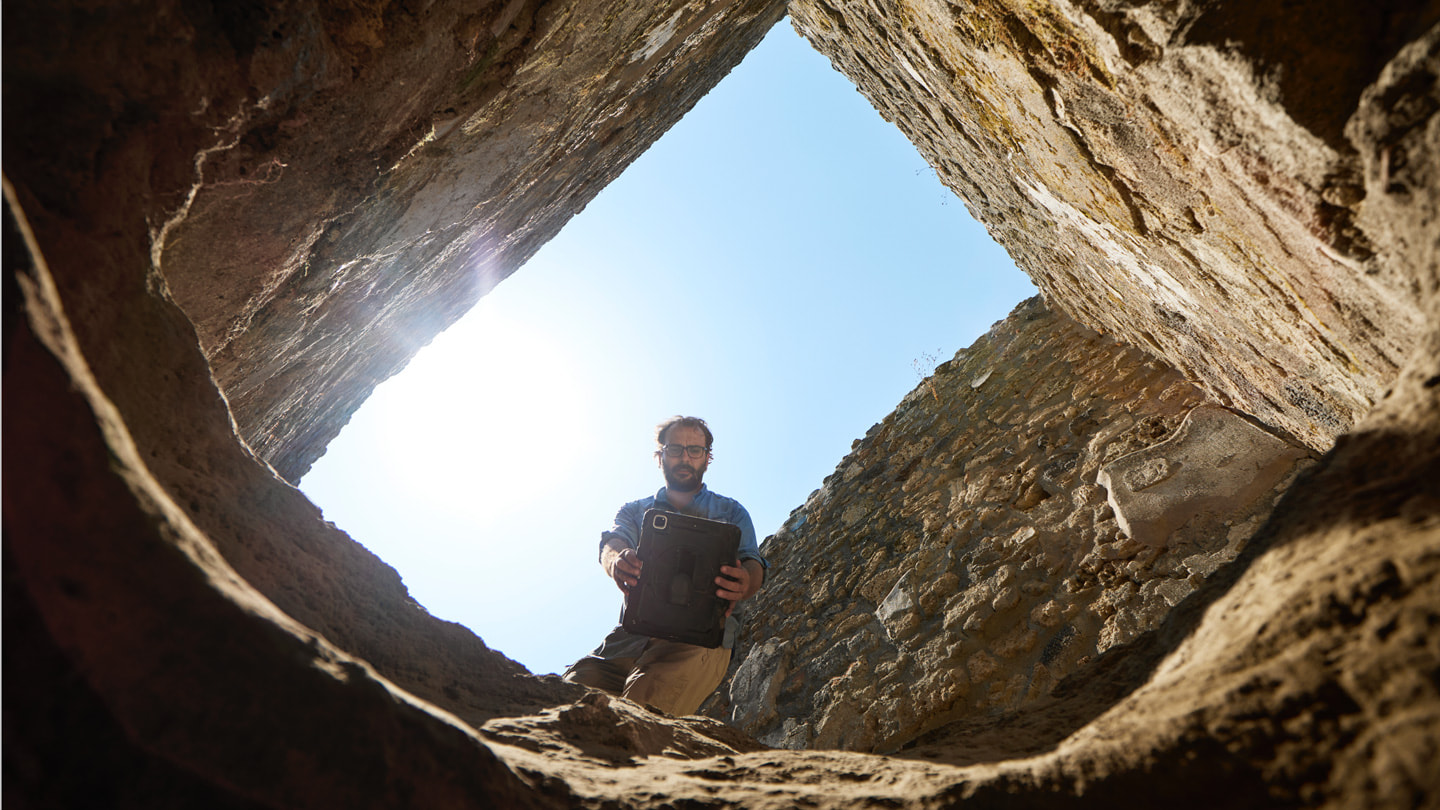 在发掘坑内仰拍的照片：Rogers 博士站在发掘坑入口处，手持 iPad Pro。