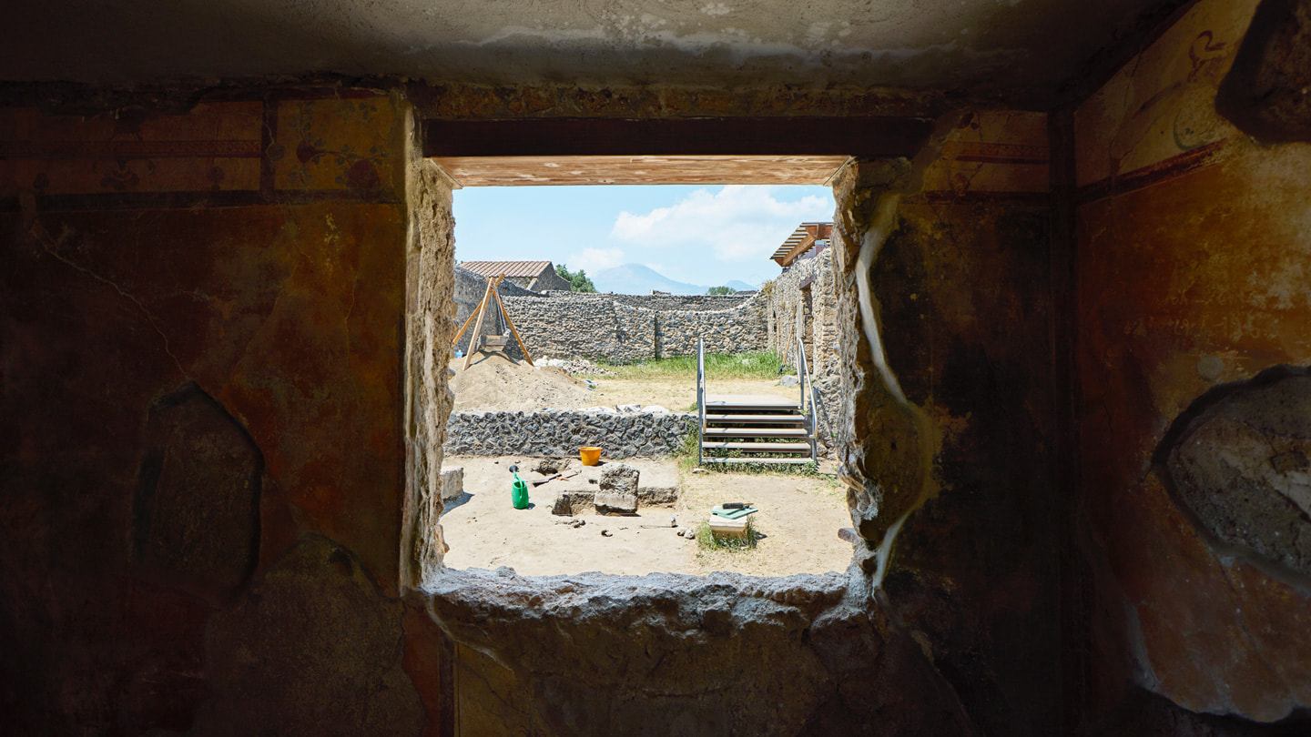 从发掘现场的窗户向外望去，可以看到石墙与远处的维苏威火山。 