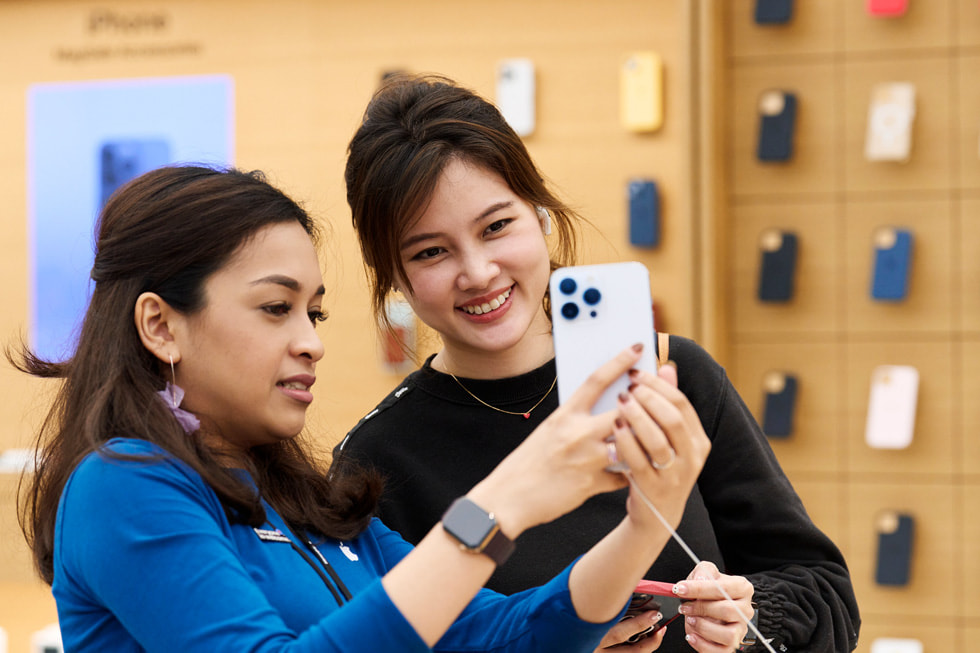 Apple Orchard Road 零售店内，一名团队成员正在向一位女性展示银色 iPhone 14 Pro。