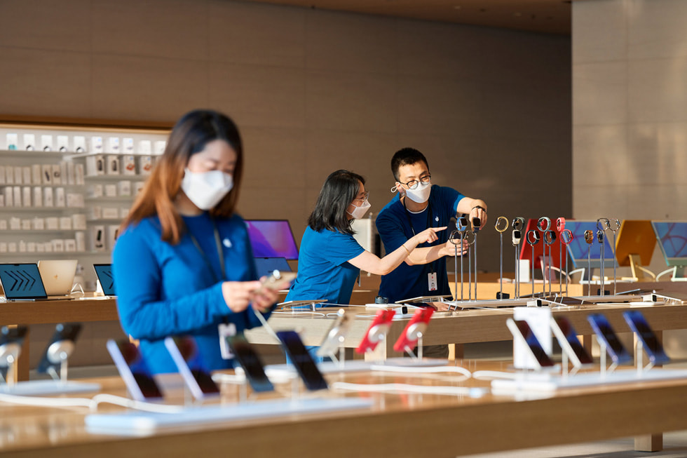 Apple 三里屯零售店内，一名团队成员注视着 iPhone。背景中，另外两名团队成员在调整 Apple Watch 展品。