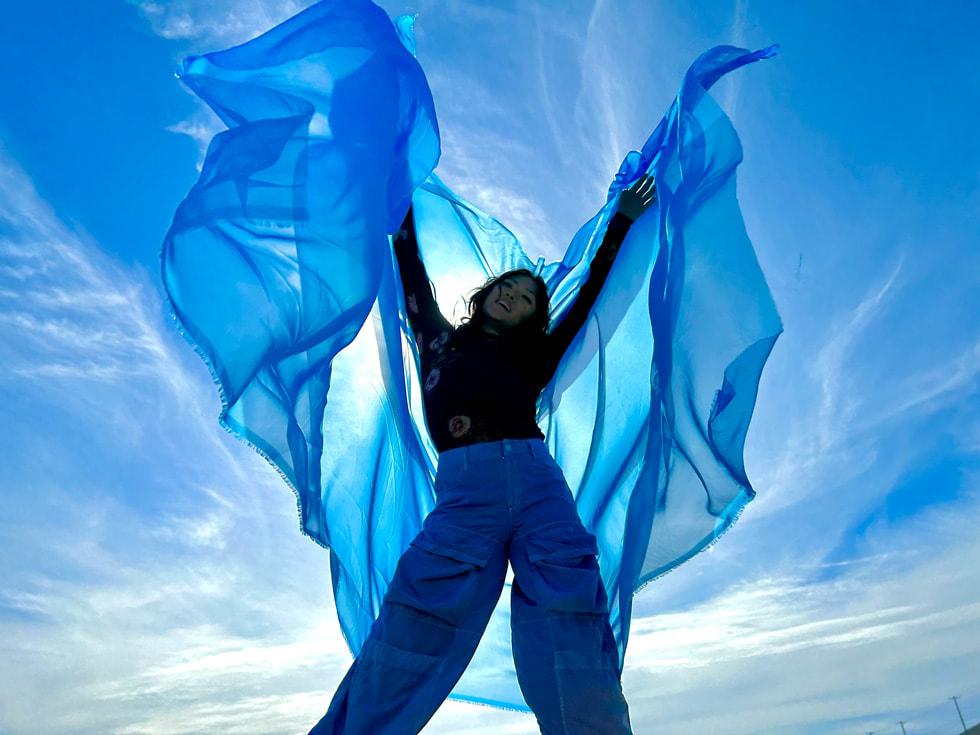 一个人在蓝天背景中手持飘动的蓝色围巾。
