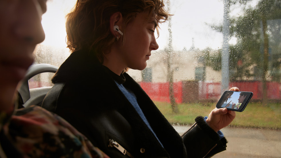 公交车上，戴着 Airpods 的女孩正使用 5G 网络在 iPhone SE 上通过同播共享功能观看视频。