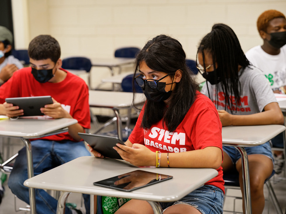 参加 Rutgers 4-H Computers Pathways 项目的学生们坐在桌旁，使用 iPad 设备。