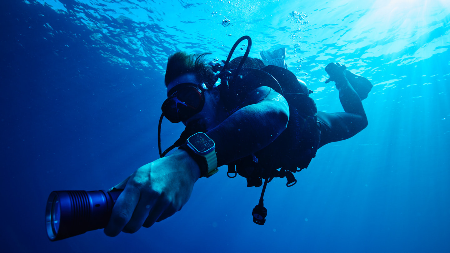 一名水肺潜水者佩戴着装有 Oceanic+ 的 Apple Watch Ultra 在海面下游泳。