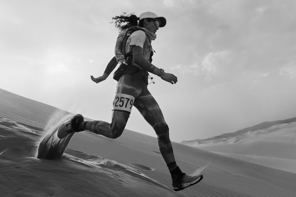 一位佩戴着 Apple Watch Ultra 和比赛号码的运动员跑下沙丘。