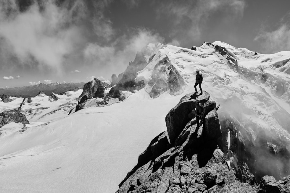 一位 Apple Watch Ultra 用户站在嶙峋的山峰，被雪山环绕。 