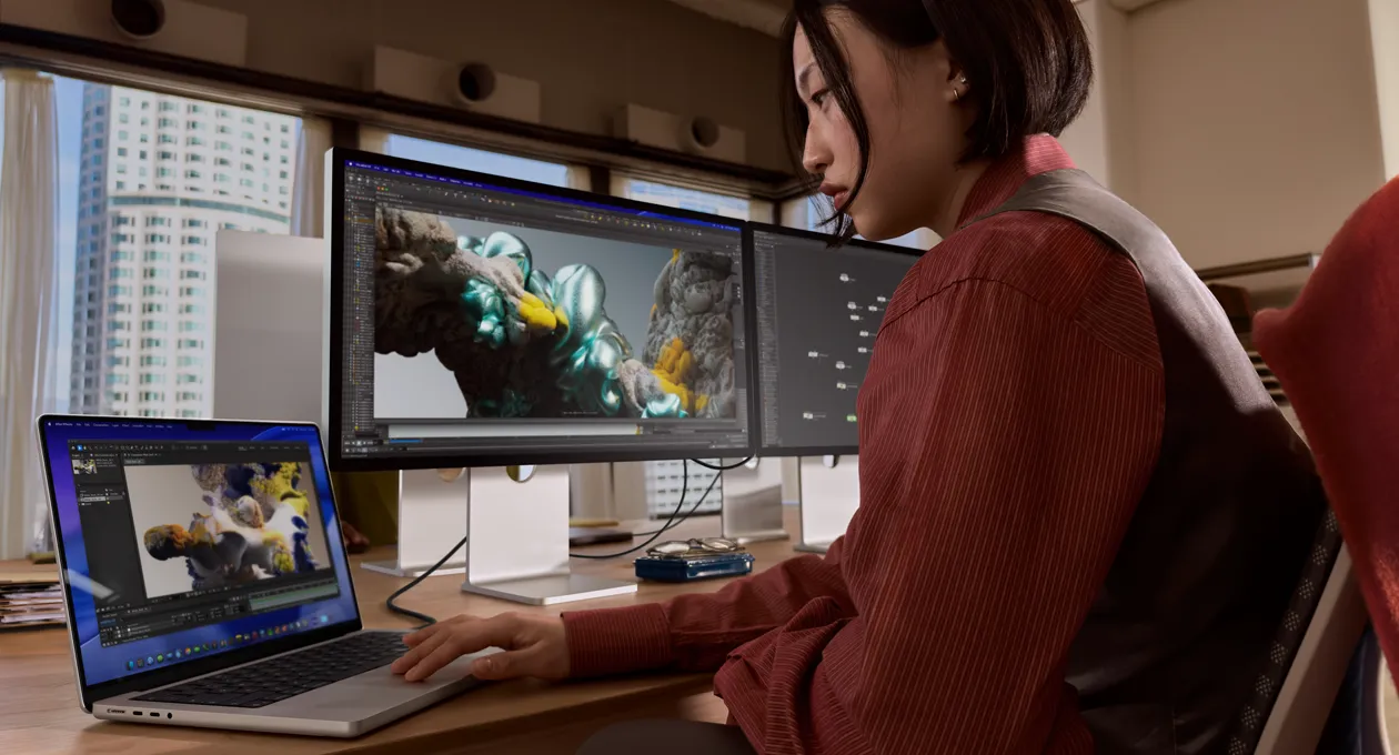 在办公室环境中，一个人在一台 MacBook 笔记本电脑上工作，笔记本电脑通过雷雳&nbsp;5 端口串联 Studio Display XDR。