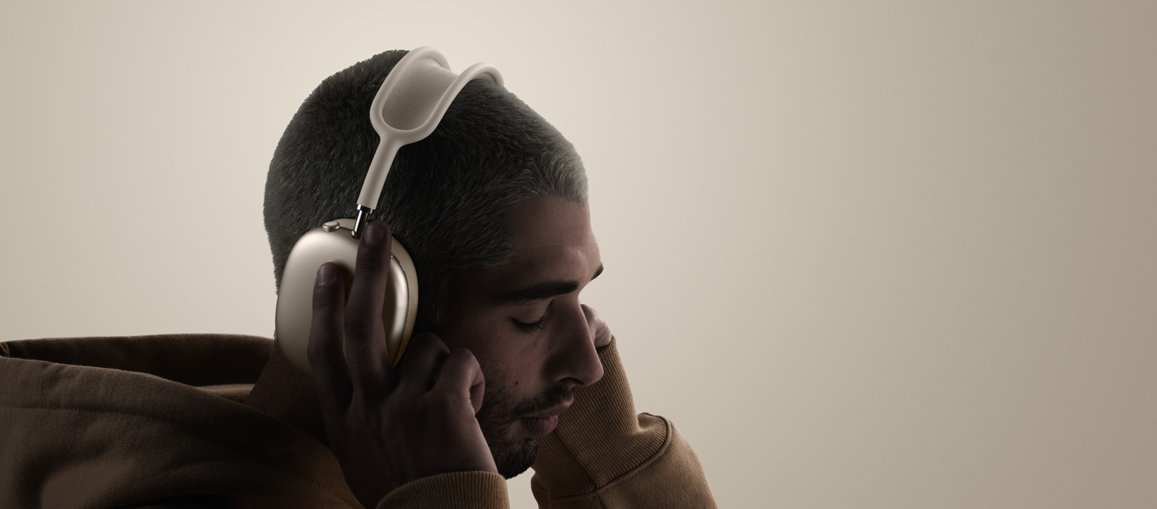 一个人头戴 AirPods Max 2 耳机，并用双手触碰耳垫，展示侧面外观。