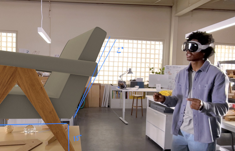 一个人戴着 Apple Vision Pro，通过手部动作对一张椅子的 3D 投影进行测量。