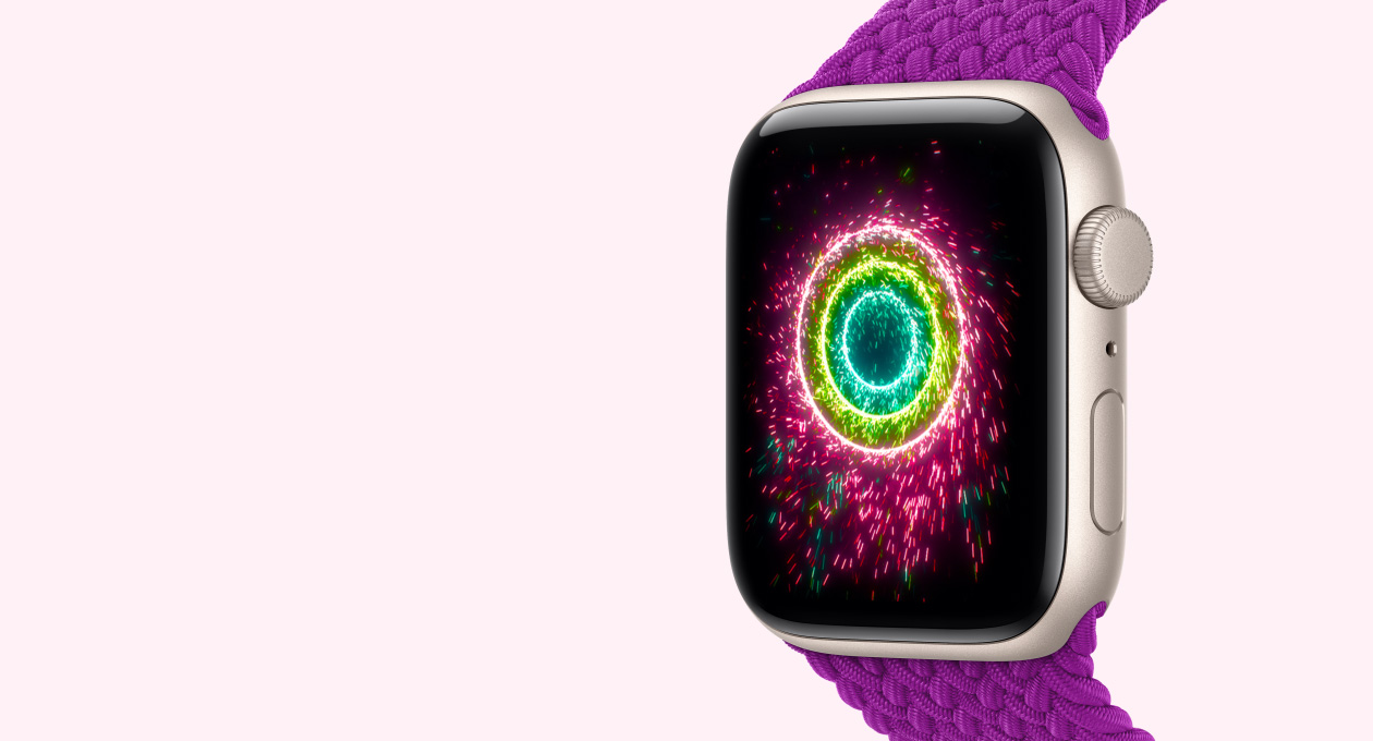 Apple Watch SE 3，展示星光色铝金属表壳搭配洋红色编织单圈表带，屏幕显示健身圆环化作火花四溅的仙女棒形态，排列成一组粉色、柠檬绿色及浅蓝色的同心圆环。
