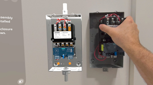 一只手将接有电线的机械盒安装在墙上，旁边有 3D 成像的同款设备。