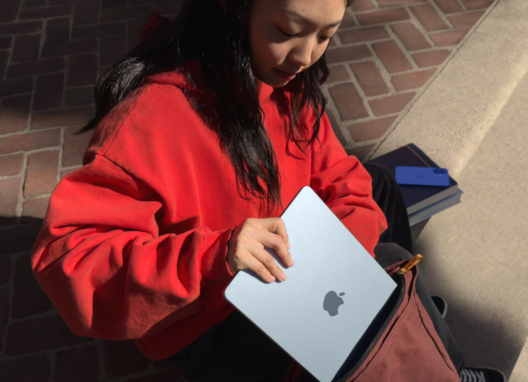 一个人坐在石阶上，正在将 MacBook 放入背包