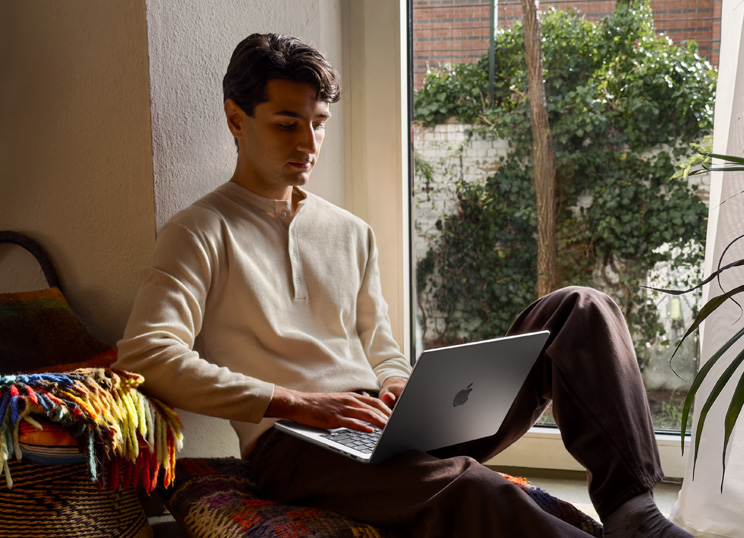 一个人坐在窗边的地板上使用 MacBook
