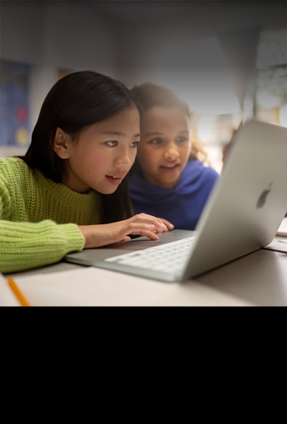 教室里，两位年幼的学生坐在桌前，神情专注地使用 MacBook 开展协作。