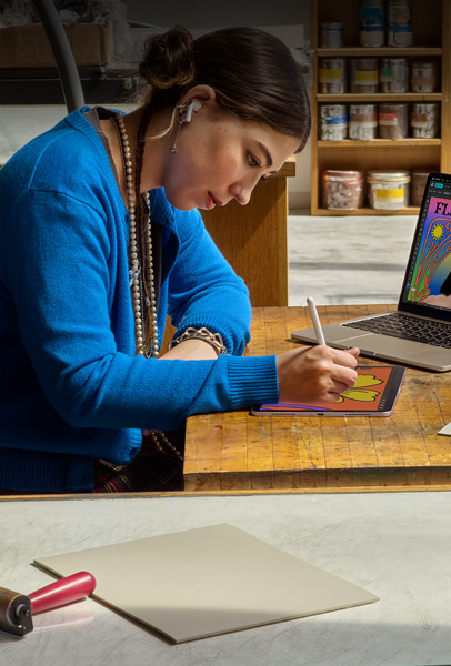 两名学生在宿舍内用银色的 MacBook 浏览内容，其中一人坐在床上，另一个人拿着设备坐在地板上。