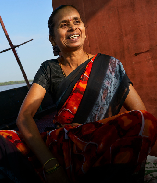一位印度女子坐在船上微笑，背景是航行水道。