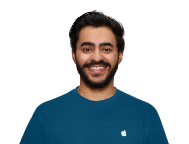 一位 Apple Store 零售店 Specialist 专家，身穿带有 Apple 标志的蓝色上衣，面带微笑。