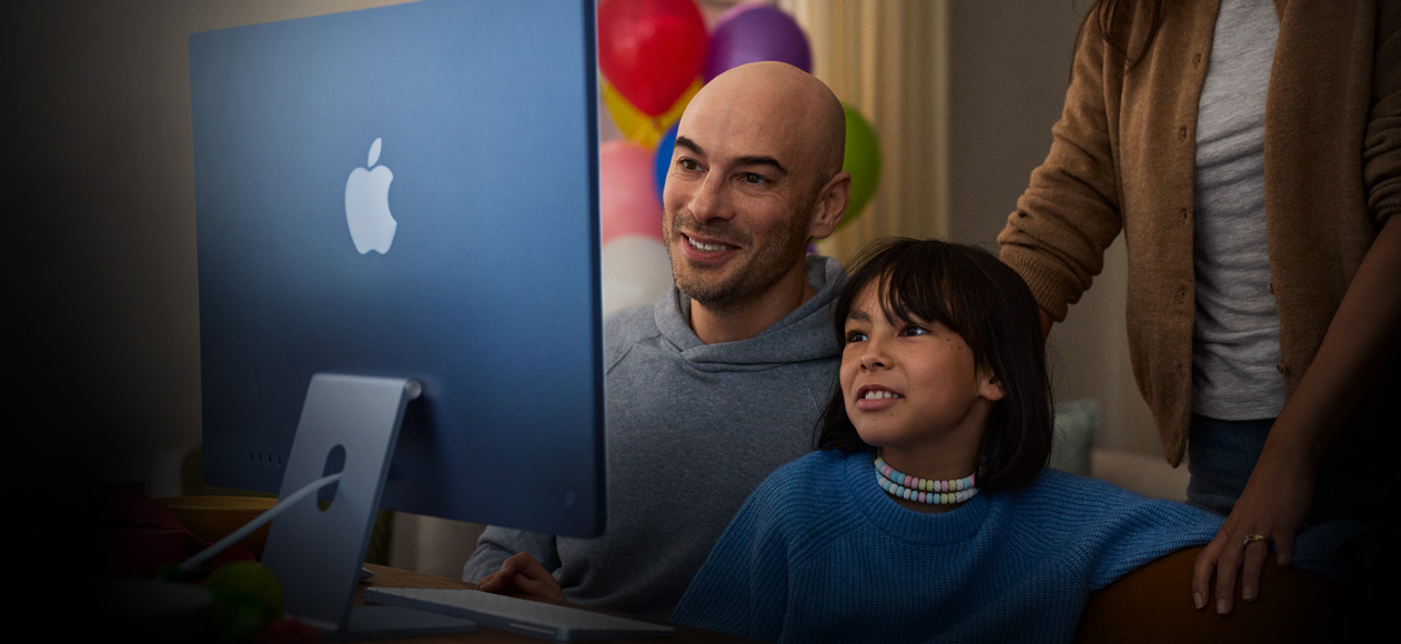 两个人坐在一起使用 iMac，第三个人站在他们身后观看。