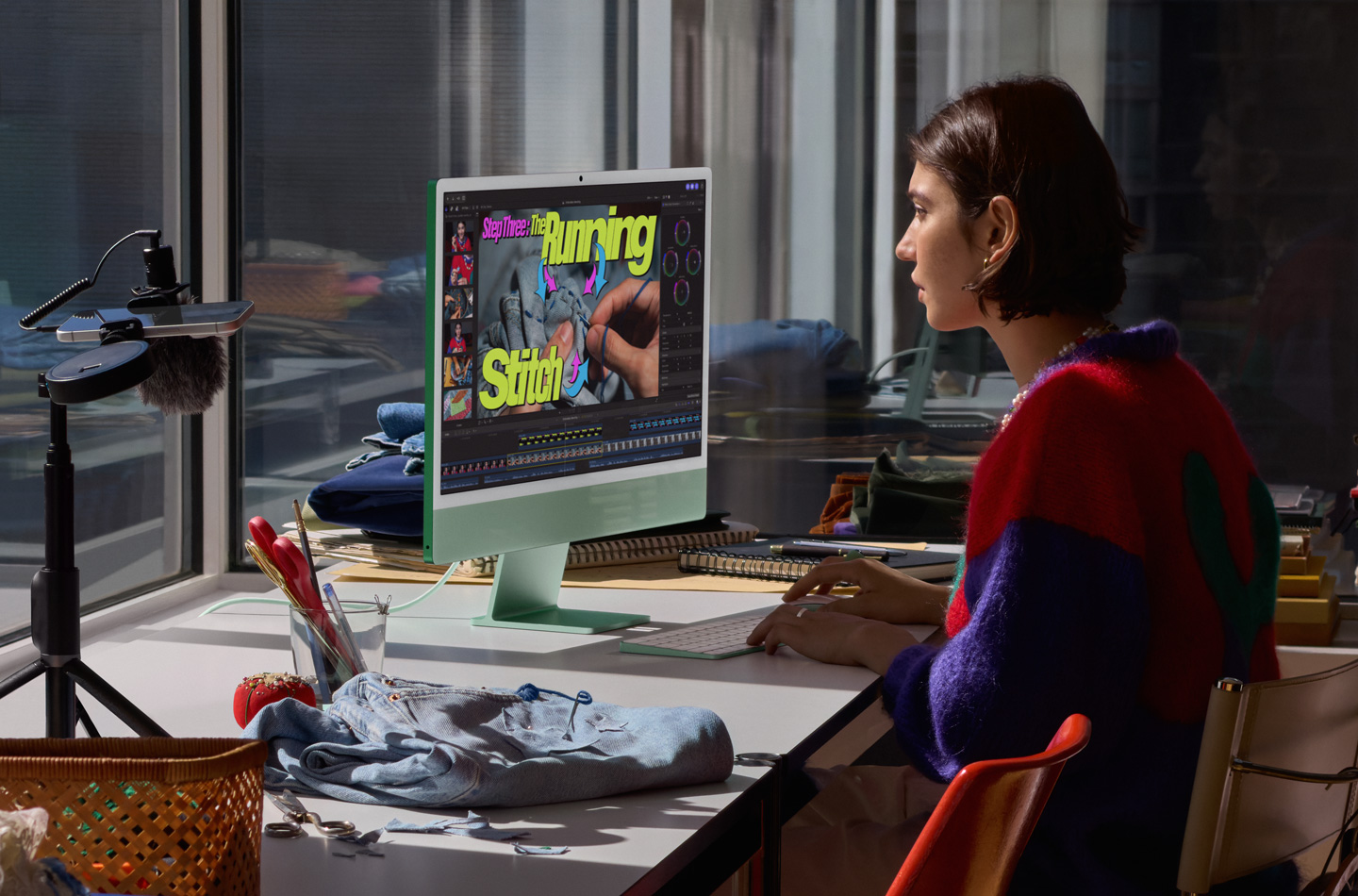 一个人在桌前使用绿色 iMac，边用妙控键盘打字和使用妙控鼠标，边观看縫纫教程。