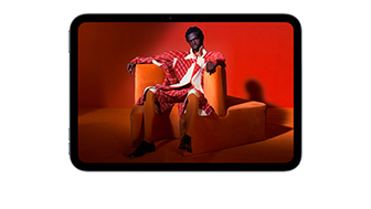 iPad mini 的正面视图，屏幕展示橙色房间内，一个身穿橙色西装的人坐在橙色椅子上，画面生动鲜活。
