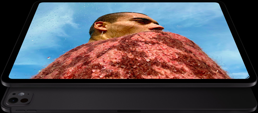 横屏放置的深空黑色 iPad Pro 正面斜侧外观，展示圆角设计、黑色显示屏边框。屏幕显示一张照片：蓝天下的男子身穿红色毛衣。下方是另一部横屏放置的深空黑色 iPad Pro，背面外观展示 Pro 级摄像头系统、音量增大按钮和音量减小按钮。