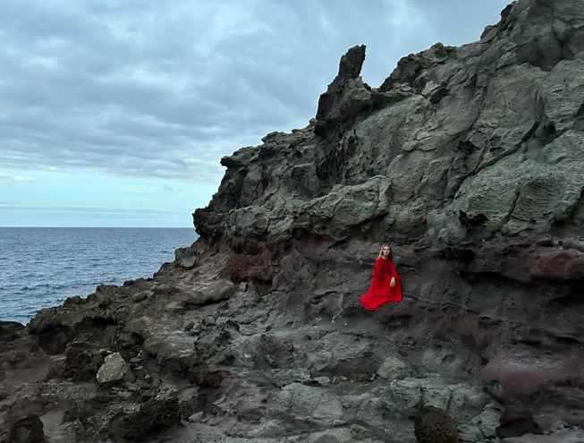 主摄像头在低光环境下拍摄的照片，一身红色长裙的女子，站在陡峭的岩壁中。