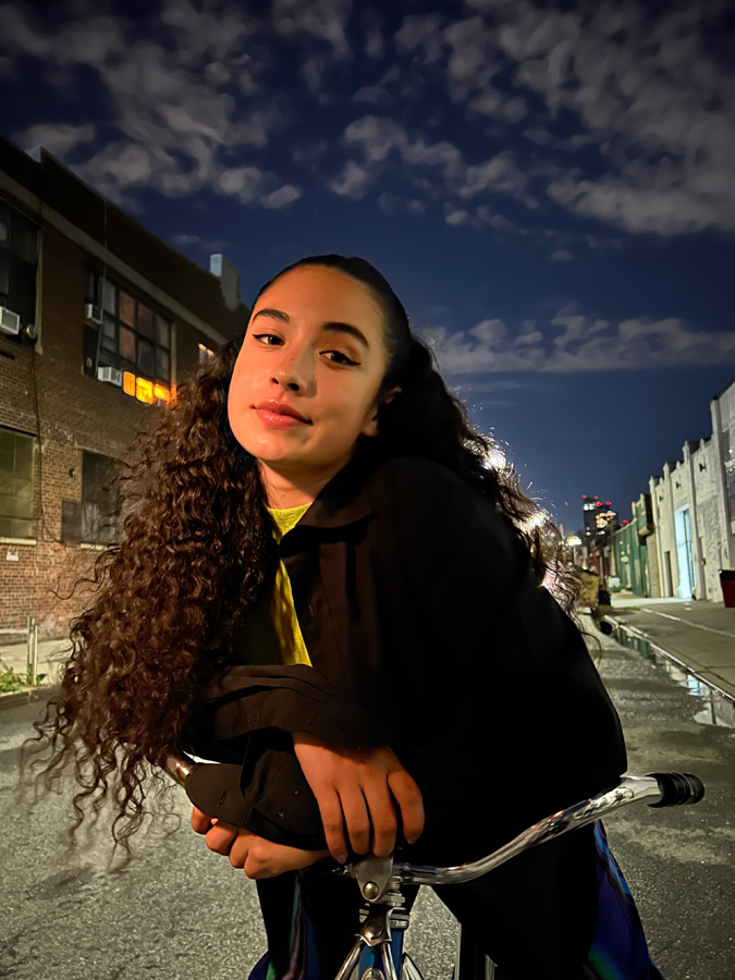 夜间模下拍摄的照片，夜晚的城市街道上，一个姑娘骑在单车上看向镜头。