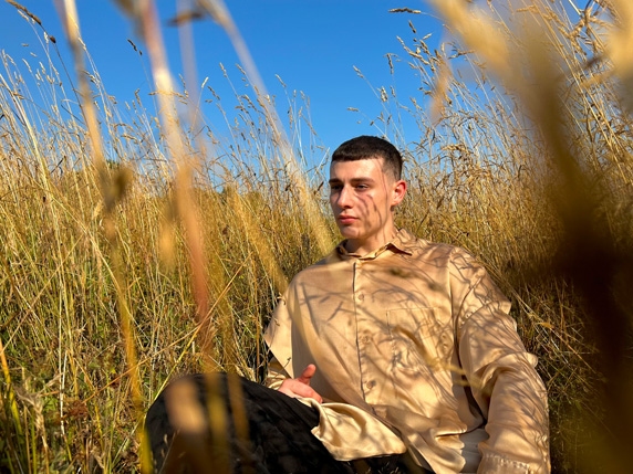 智能 HDR 4 效果的照片，一名青年男子坐在田野中，身后是湛蓝的天空。