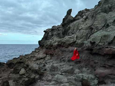 海边的灰色岩壁衬托着一名红衣人的惊艳照片，以 Pro 水准主摄拍摄。