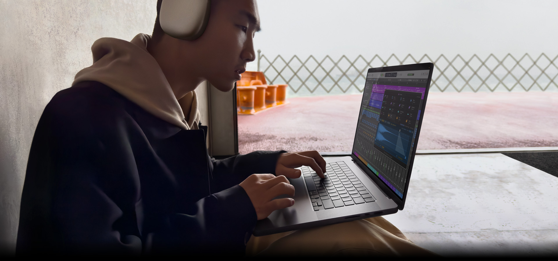一个人头戴 AirPods Max 的侧面图，他正在 16 英寸 MacBook Pro 上使用 Logic Pro，屏幕展示 Logic Pro 工作区。