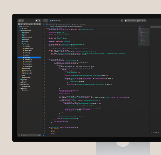 Studio Display，屏幕显示打开的 Xcode app，展示彩色的代码编辑器，运行 app 测试的 iPhone 在屏幕右侧部分可见。