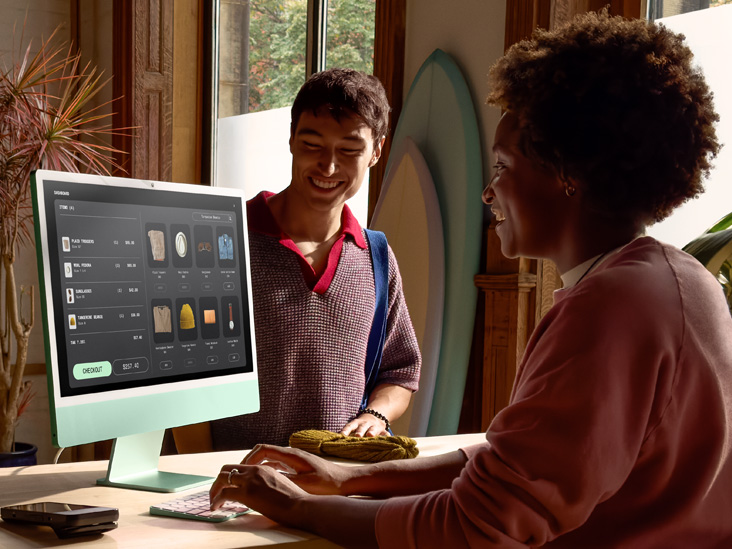 光线充足的房间内有两人，其中一人正在一部配备 M4 芯片的绿色 iMac 上查看订单。