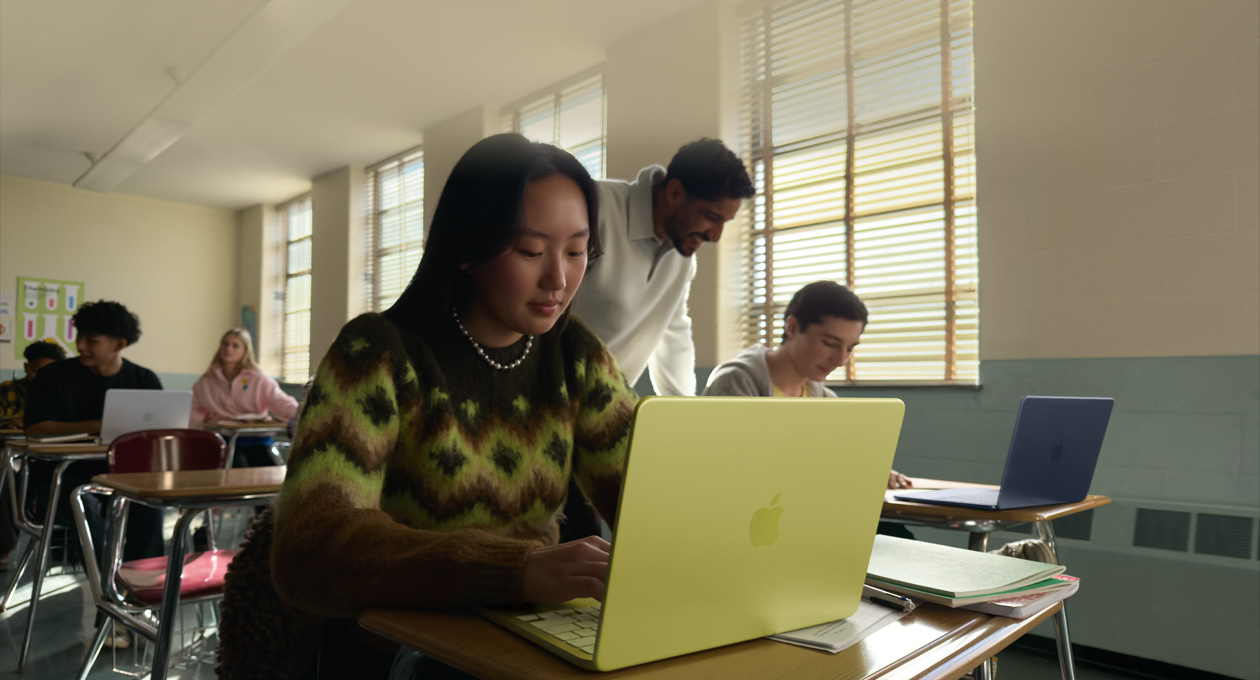 一名学生在教室里使用未接电源的柑橘黄色 MacBook Neo。