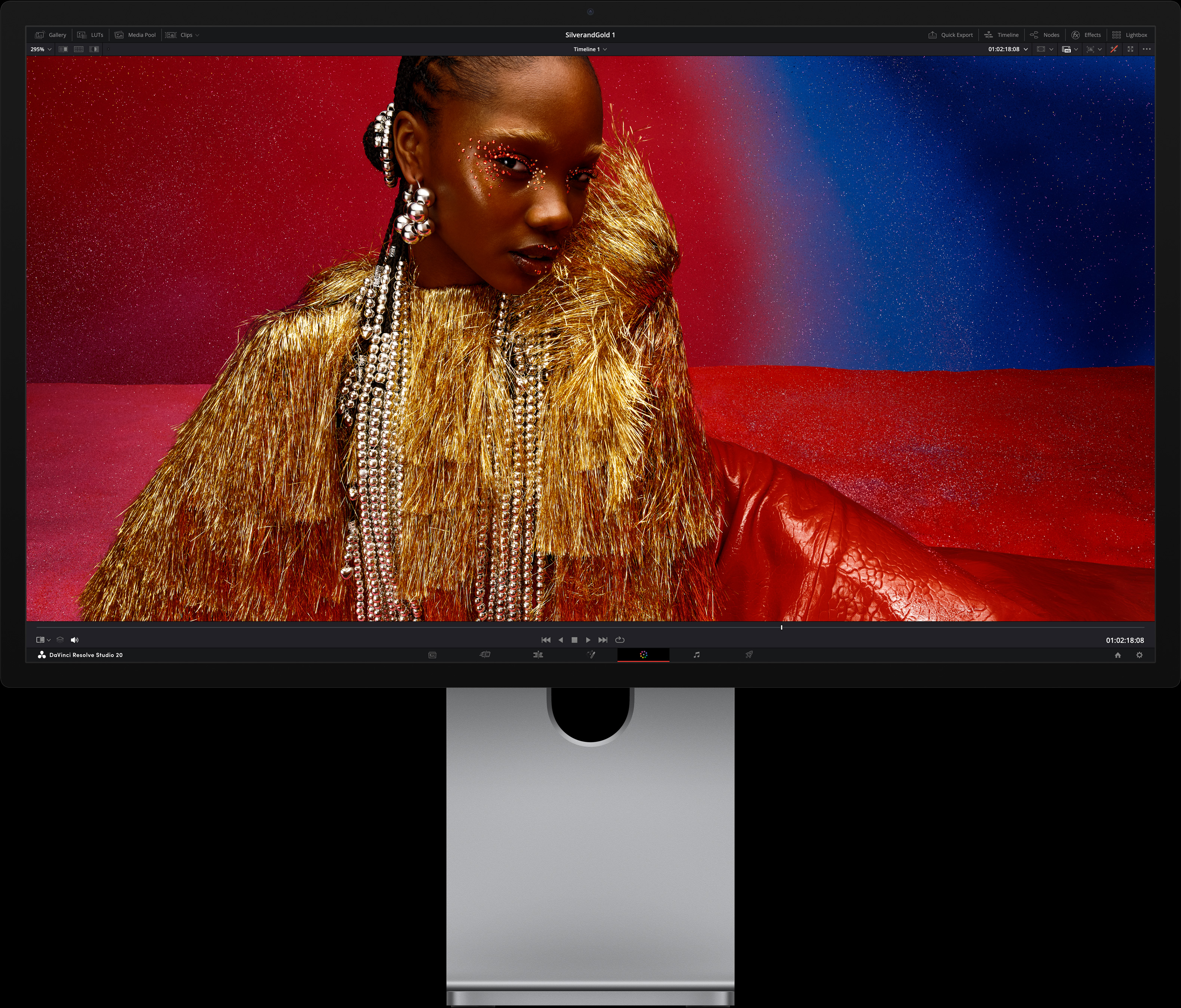 一个人身着亮红色服装，搭配金属质感的超大配饰，坐在蓝色和红色渐变的背景前，展示 Studio Display XDR 实现的画质。