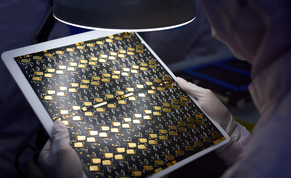 工人戴着手套在带放大镜的检验灯下检查电路板